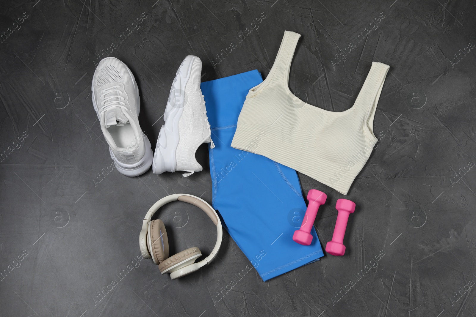 Photo of Stylish sportswear, white sneakers, dumbbells and headphones on grey background, flat lay