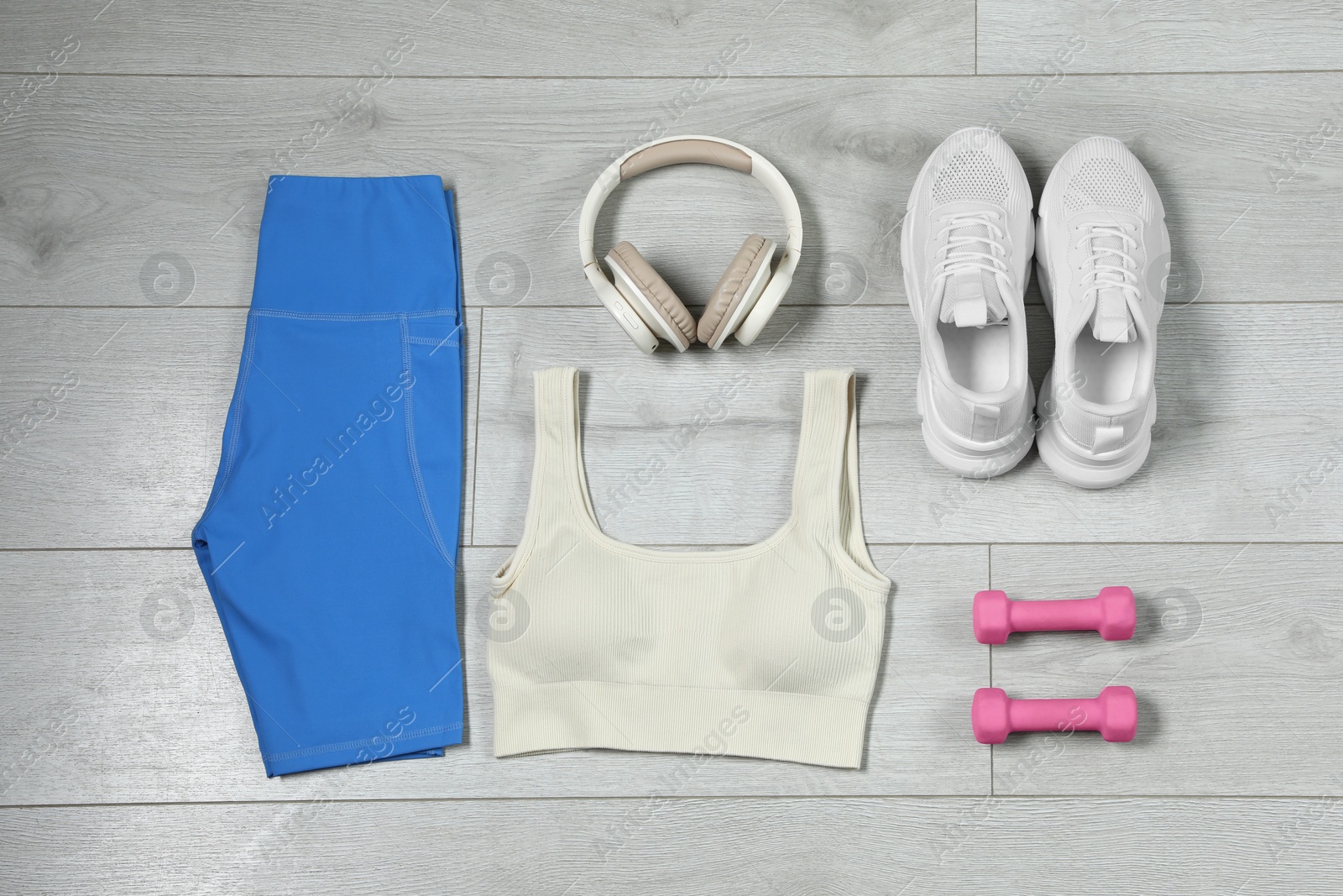 Photo of Stylish sportswear, white sneakers, dumbbells and headphones on wooden background, flat lay