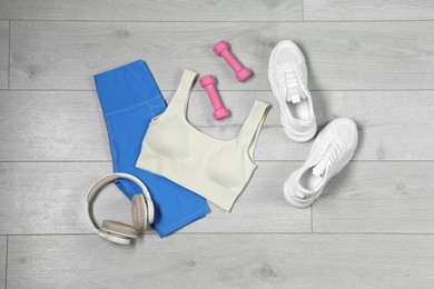 Photo of Stylish sportswear, white sneakers, dumbbells and headphones on wooden background, flat lay