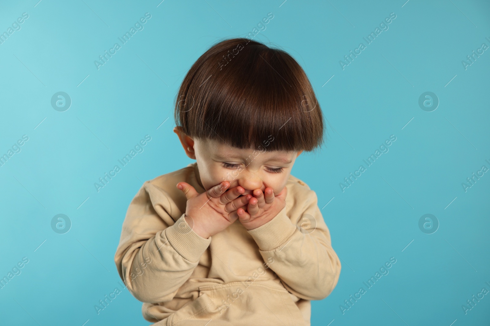 Photo of Portrait of emotional little boy covering mouth on light blue background