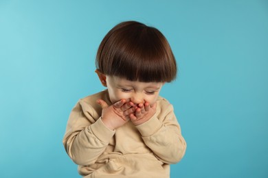 Photo of Portrait of emotional little boy covering mouth on light blue background