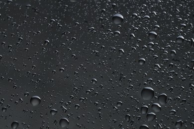 Photo of Water drops on dark grey glass surface, top view