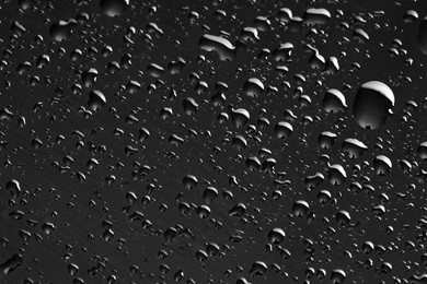 Photo of Water drops on dark grey glass surface, top view