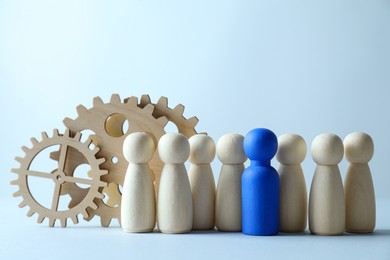 Photo of Human resources concept. Blue figure among wooden ones and gearwheels on light background, closeup. Space for text