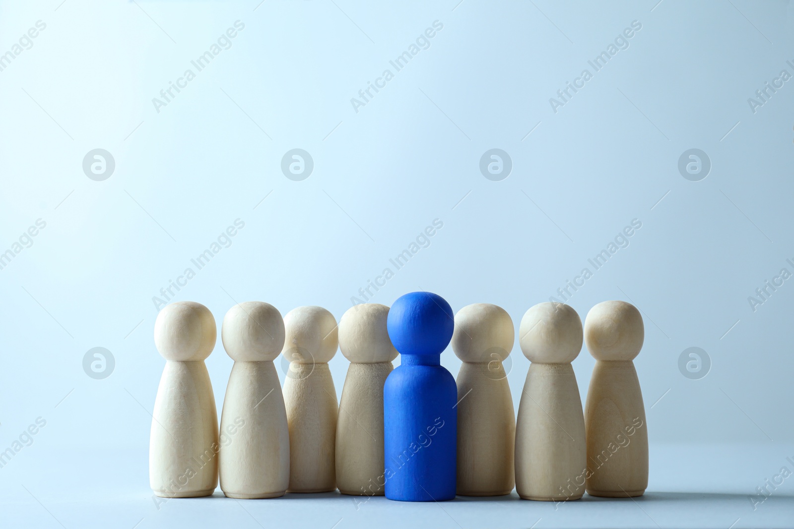 Photo of Human resources concept. Blue figure among wooden ones on light background, closeup. Space for text