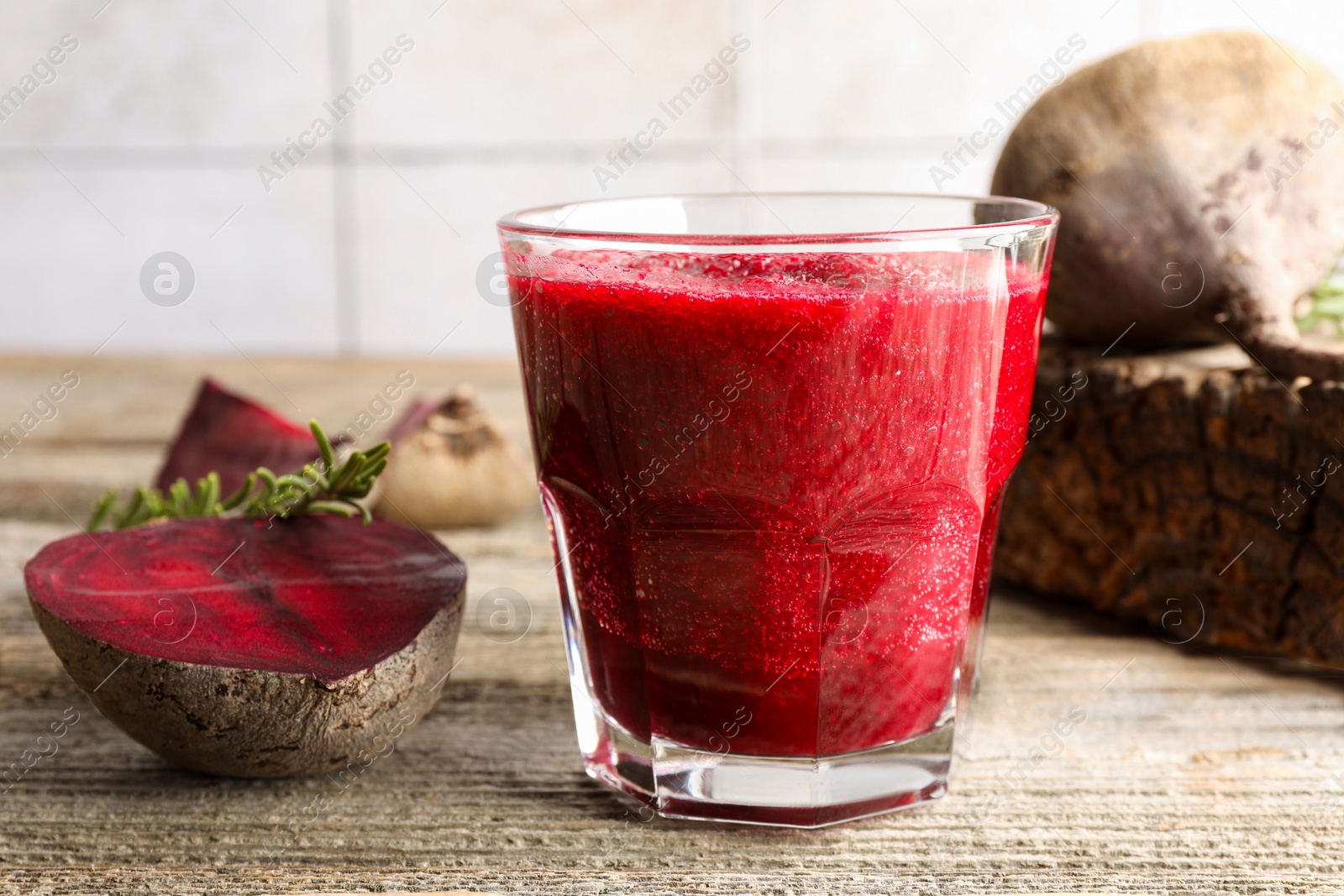 Photo of Fresh beetroot smoothie in glass, rosemary and cut vegetables on wooden table, closeup