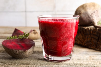 Photo of Fresh beetroot smoothie in glass, rosemary and cut vegetables on wooden table, closeup