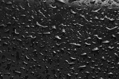 Photo of Water drops on dark grey glass surface, top view