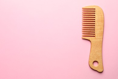 Photo of One wooden hair comb on pink background, top view. Space for text