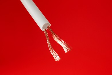 Photo of Stripped electrical wire with copper strands on red background, closeup