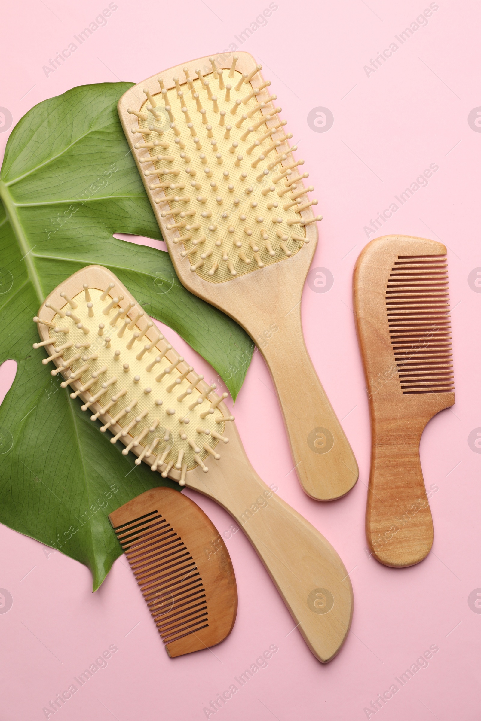 Photo of Wooden hair brushes, combs and monstera leaf on pink background, flat lay