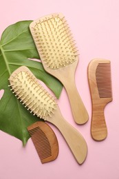 Photo of Wooden hair brushes, combs and monstera leaf on pink background, flat lay