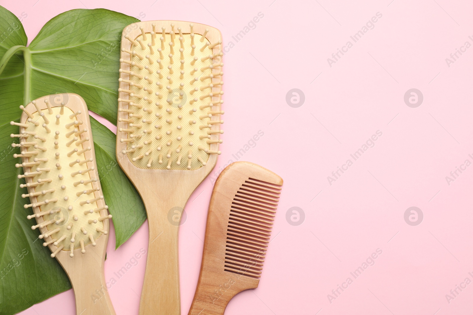 Photo of Wooden hair brushes, comb and monstera leaf on pink background, flat lay. Space for text