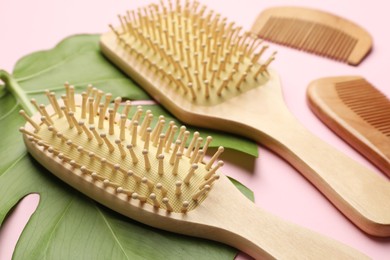 Photo of Wooden hair brushes, combs and monstera leaf on pink background, closeup