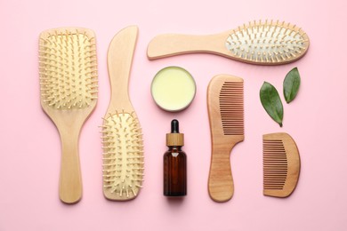 Photo of Wooden hair brushes, combs, cosmetic products and green leaves on pink background, flat lay