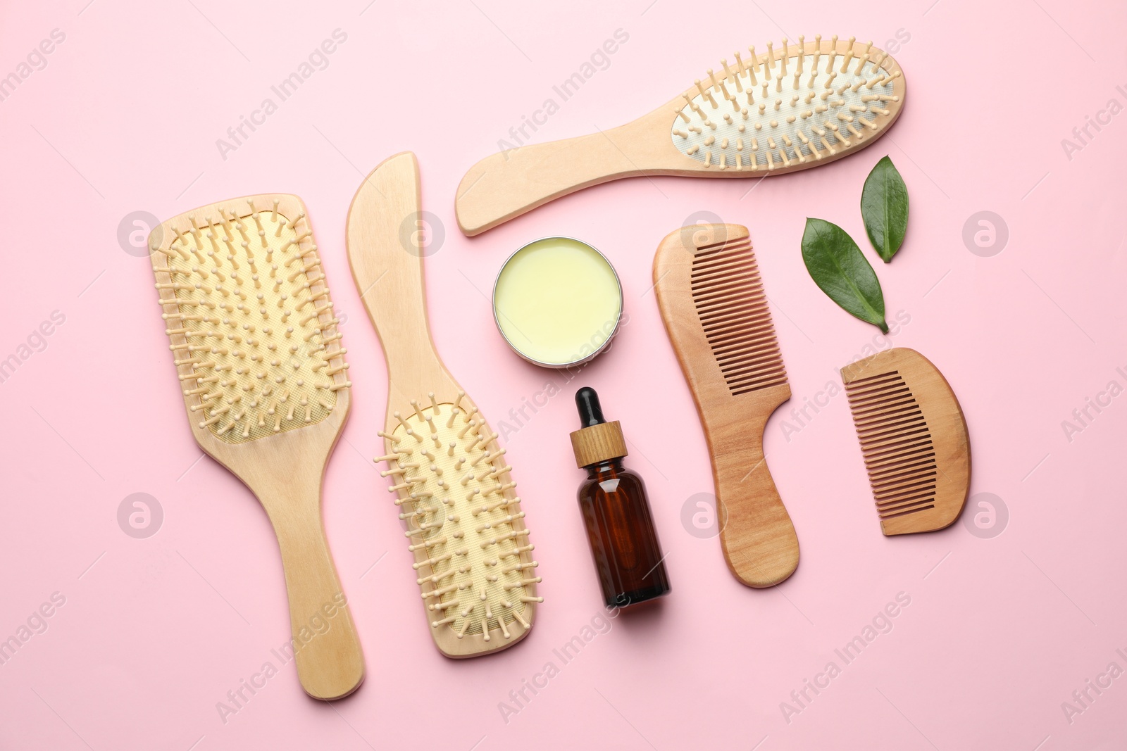 Photo of Wooden hair brushes, combs, cosmetic products and green leaves on pink background, flat lay