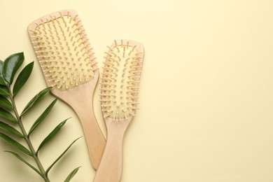 Photo of Wooden hair brushes and green branch on beige background, flat lay. Space for text