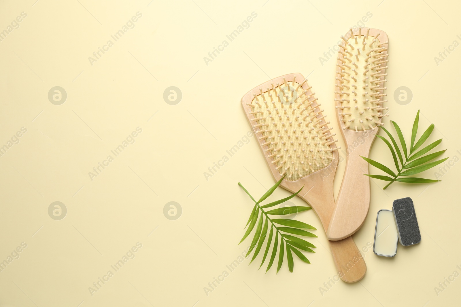 Photo of Wooden hair brushes, wax and green leaves on beige background, flat lay. Space for text