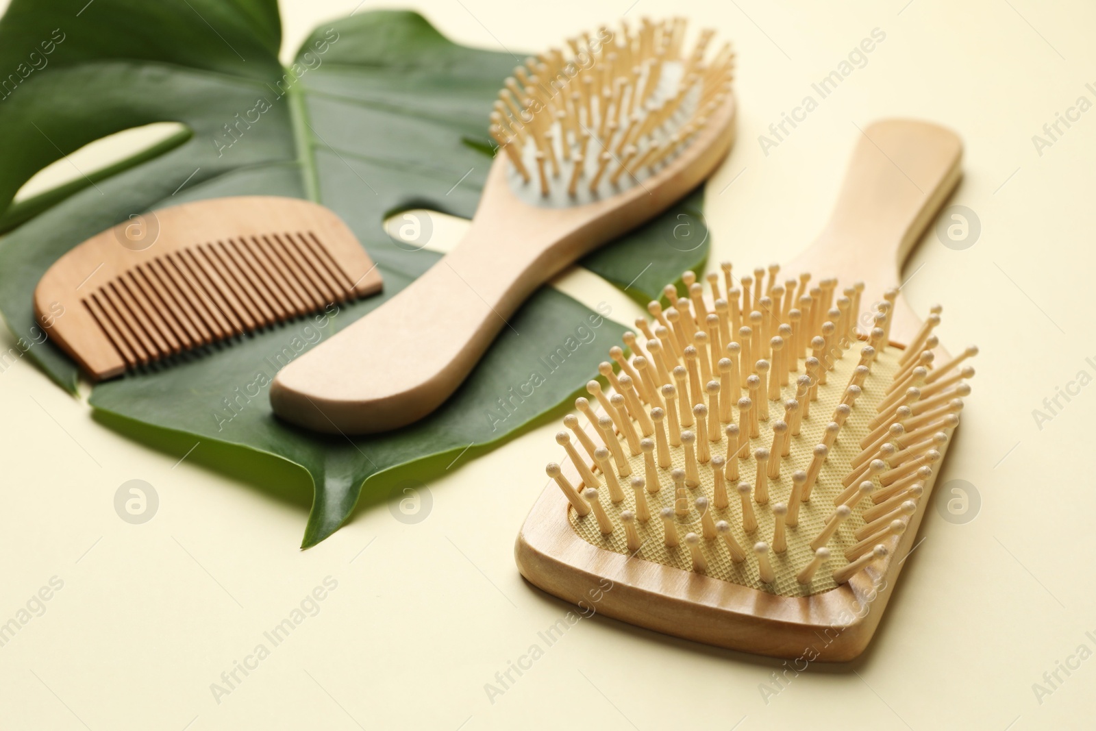 Photo of Wooden hair brushes, comb and monstera leaf on beige background, closeup