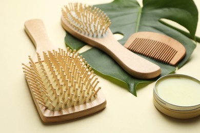 Photo of Wooden hair brushes, comb, wax and monstera leaf on beige background, closeup