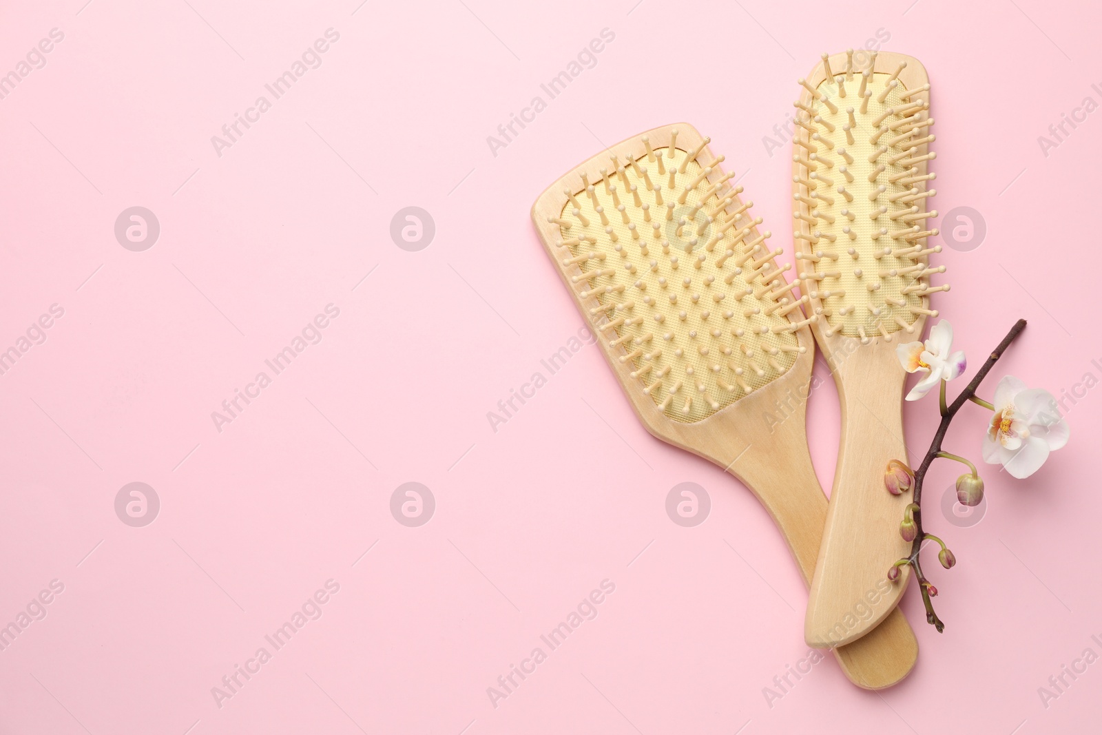 Photo of Wooden hair brushes and orchid branch on pink background, flat lay. Space for text