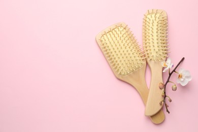 Photo of Wooden hair brushes and orchid branch on pink background, flat lay. Space for text