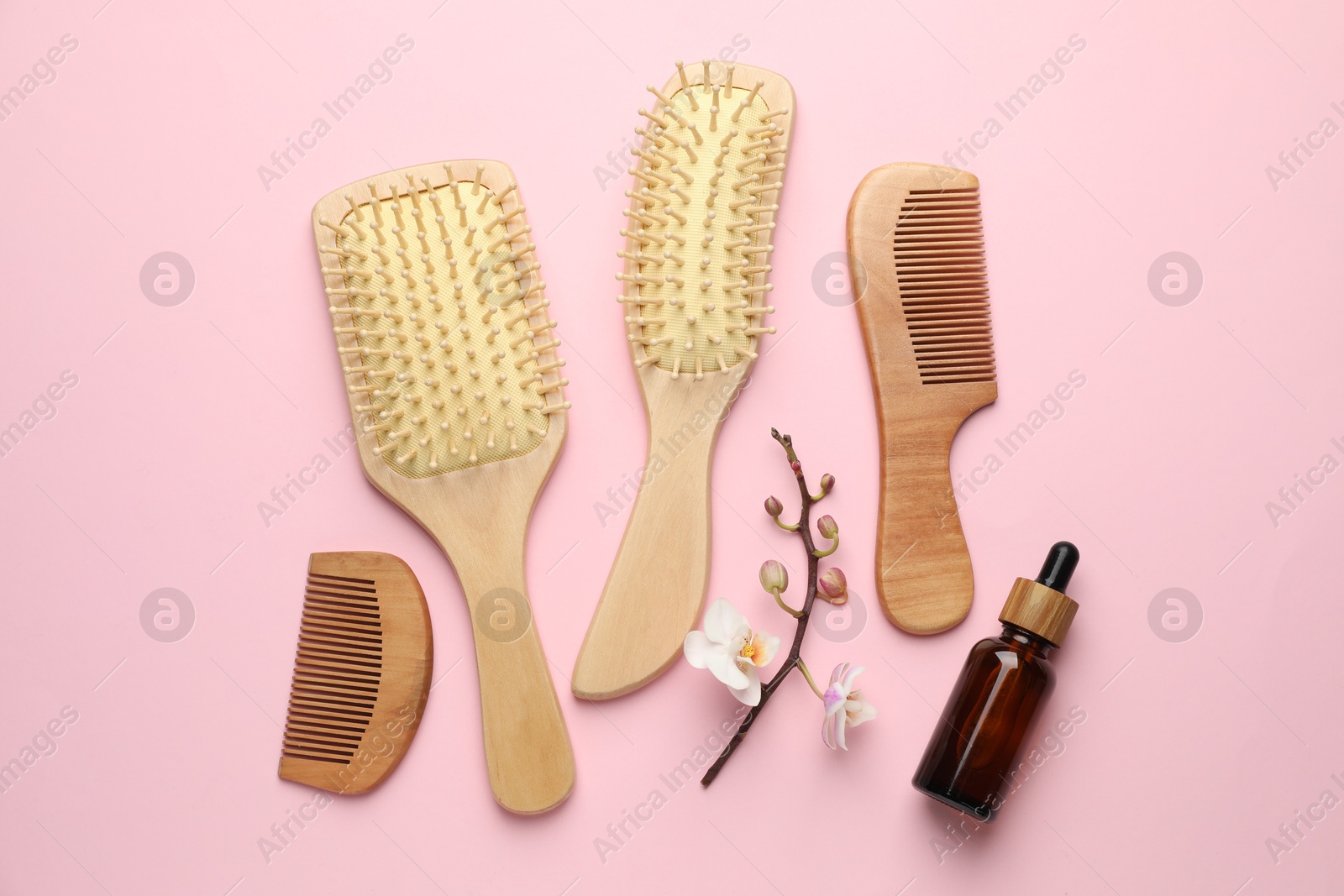 Photo of Wooden hair brushes, combs, cosmetic product and orchid branch on pink background, flat lay