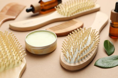 Photo of Wooden hair brushes, combs, cosmetic products and green leaves on dark beige background, closeup