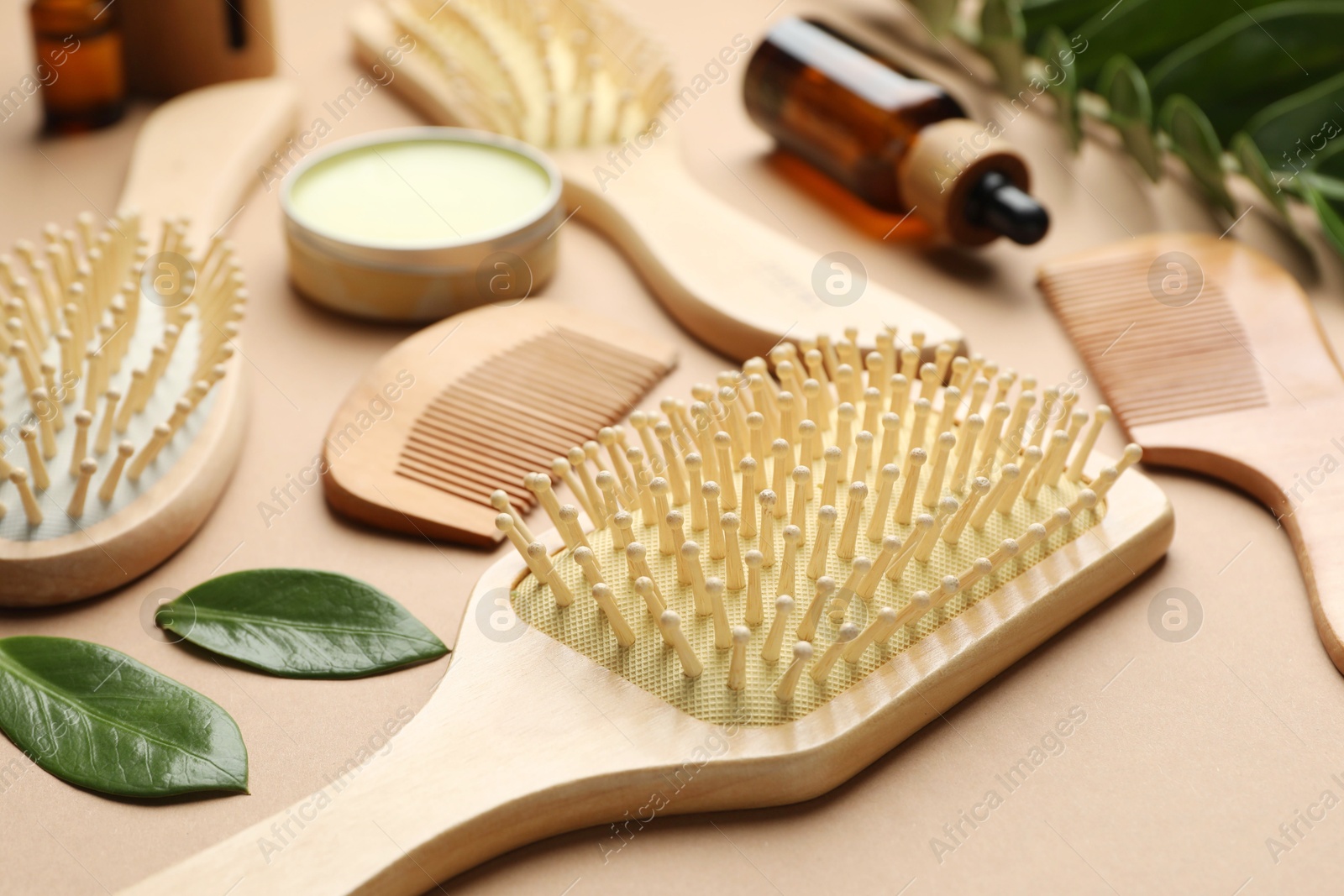 Photo of Wooden hair brushes, combs, cosmetic products and green leaves on dark beige background, closeup