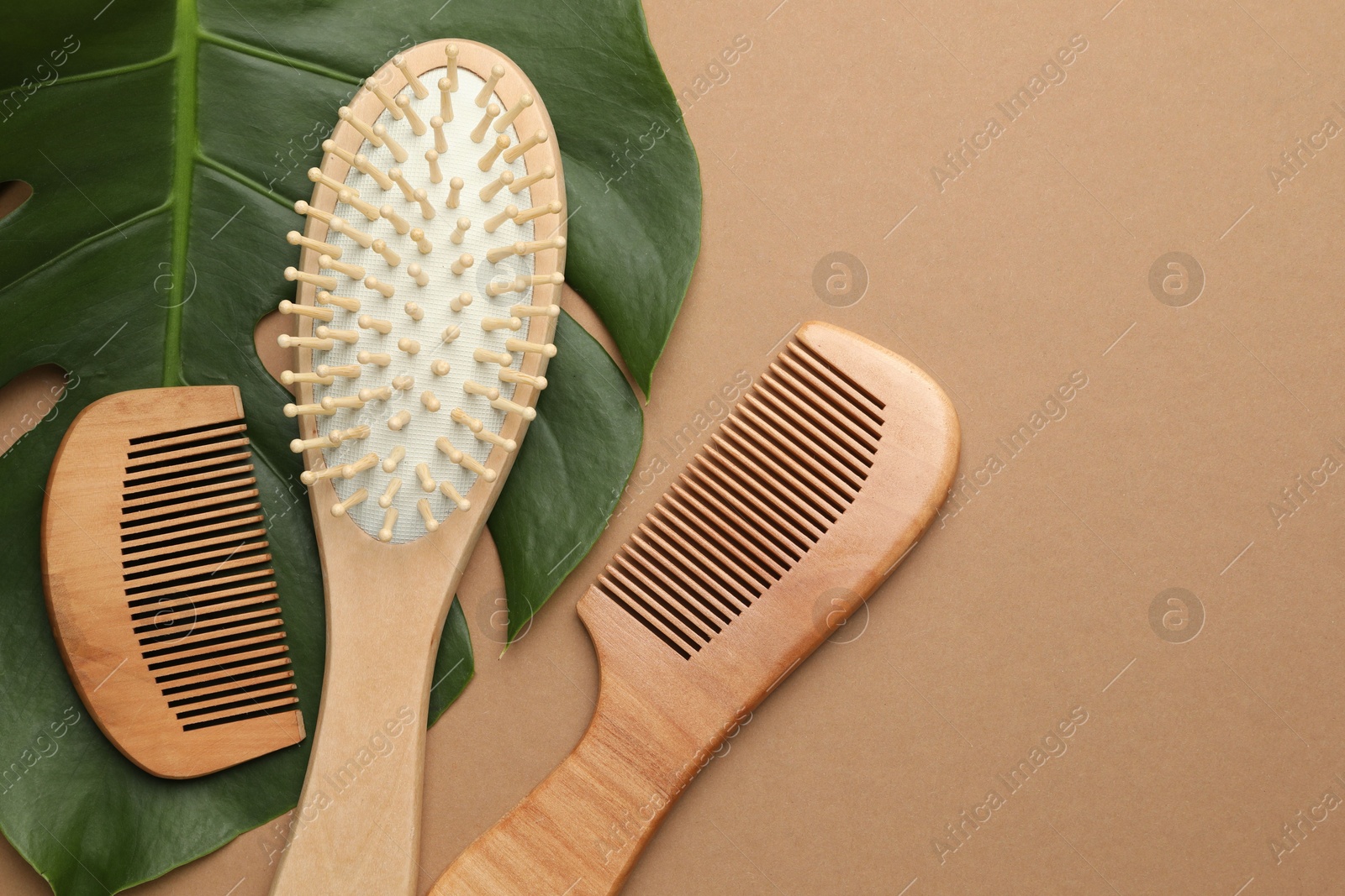 Photo of Wooden hair brush, combs and monstera leaf on dark beige background, flat lay. Space for text