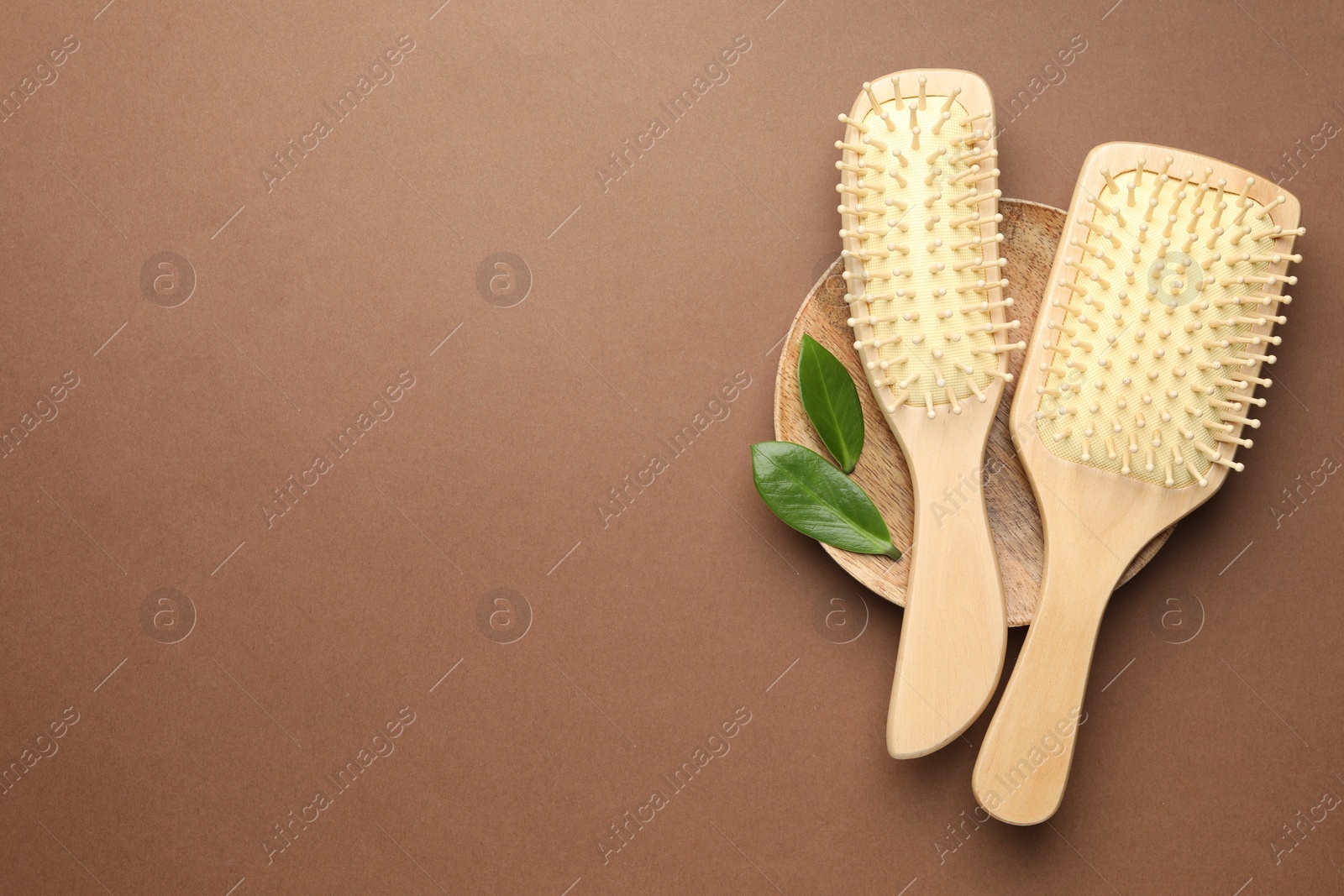 Photo of Wooden hair brushes and green leaves on dark beige background, top view. Space for text