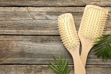 Photo of Hair brushes and green leaves on wooden table, flat lay. Space for text