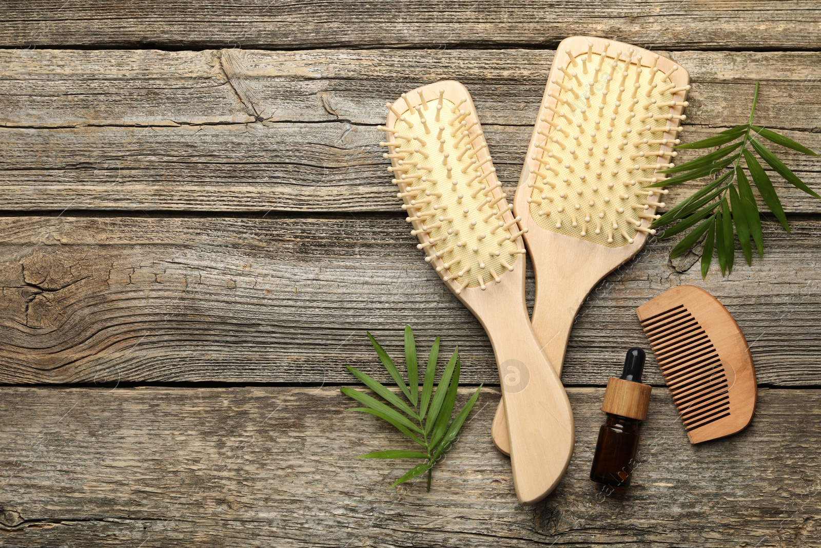 Photo of Hair brushes, comb, cosmetic product and green leaves on wooden table, flat lay. Space for text