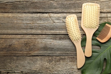 Photo of Hair brushes, comb and monstera leaf on wooden table, flat lay. Space for text