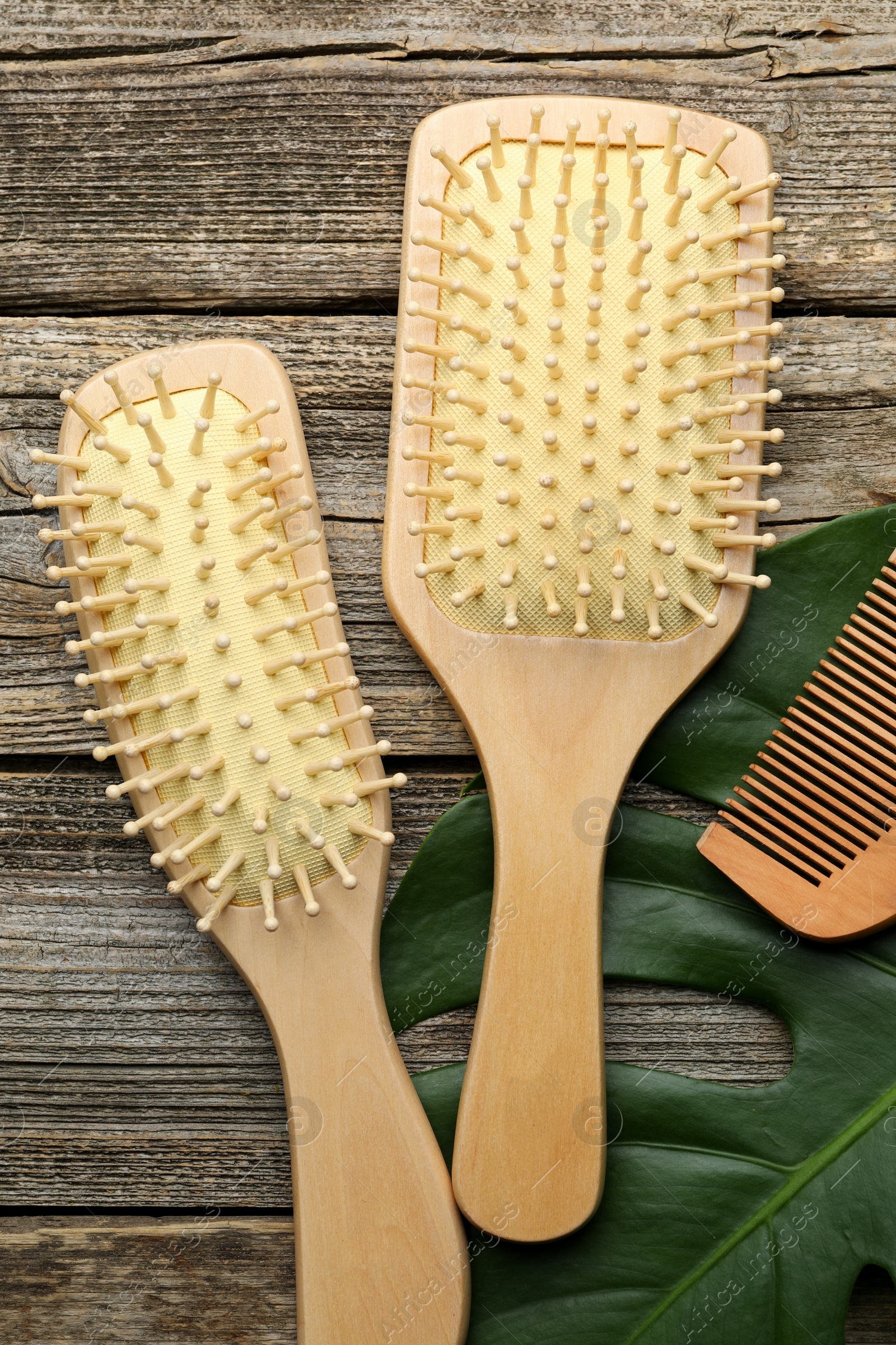 Photo of Hair brushes, comb and monstera leaf on wooden table, flat lay