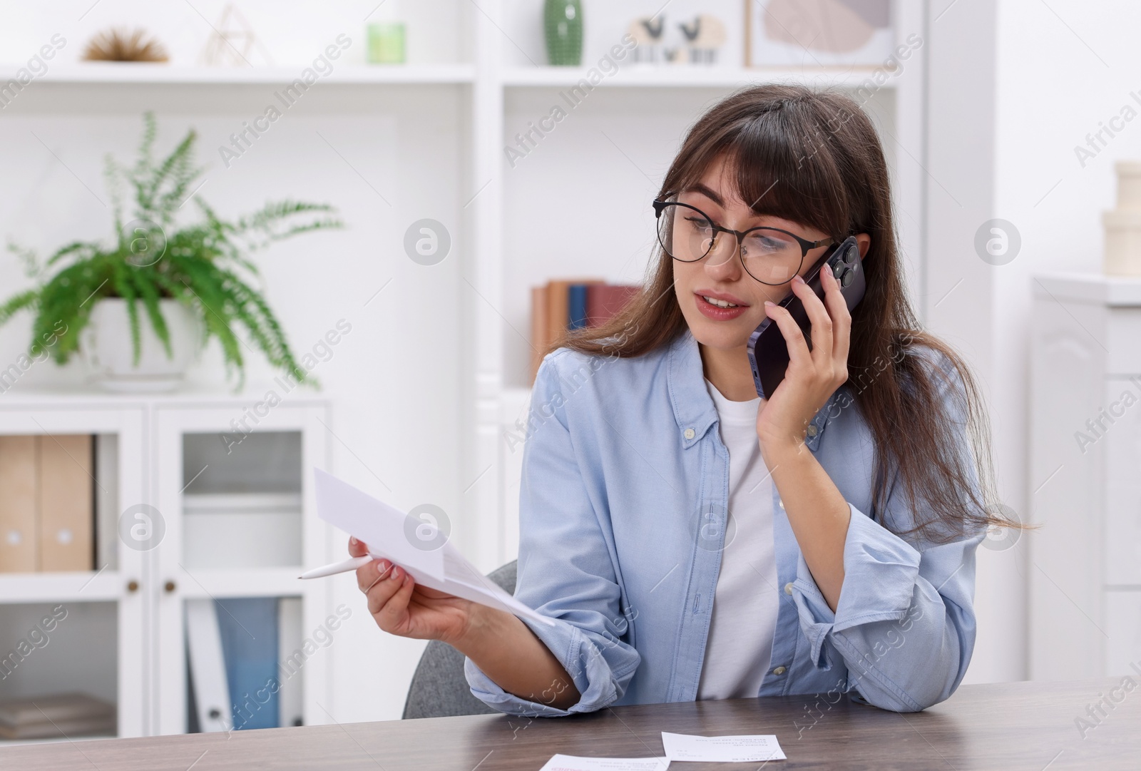 Photo of Paying bills. Woman with different invoices talking on phone at wooden table indoors