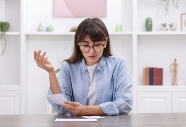 Photo of Paying bills. Woman with different invoices at wooden table indoors