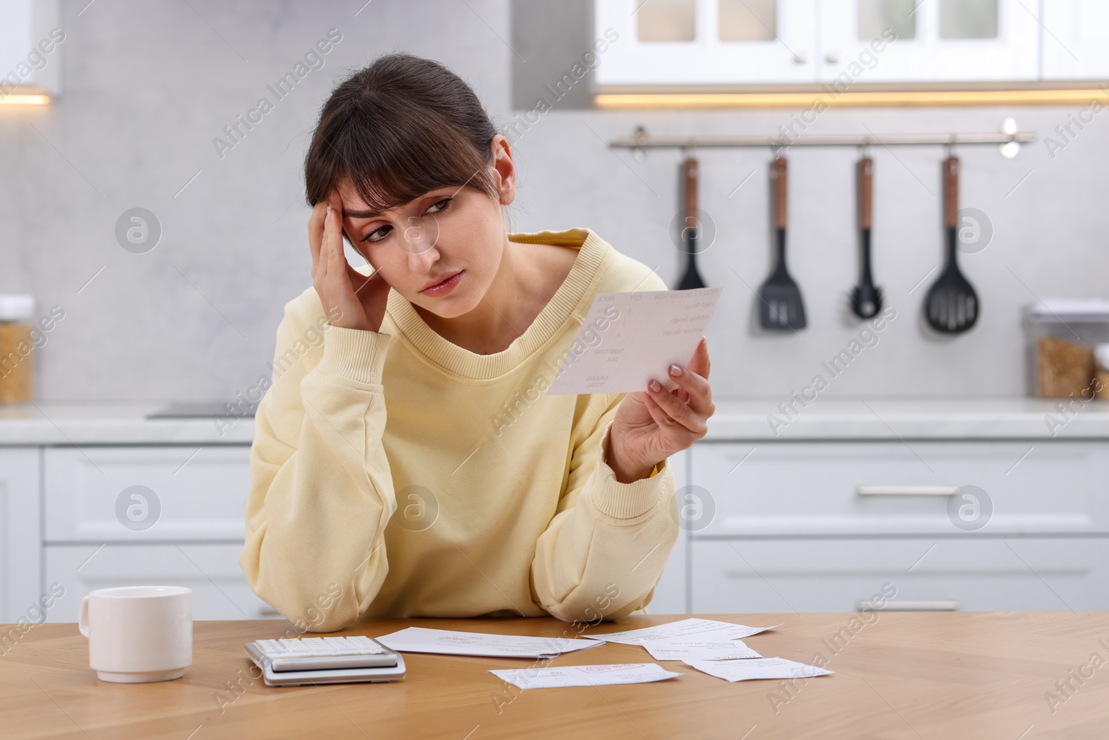 Photo of Paying bills. Upset woman with different invoices and calculator at wooden table indoors