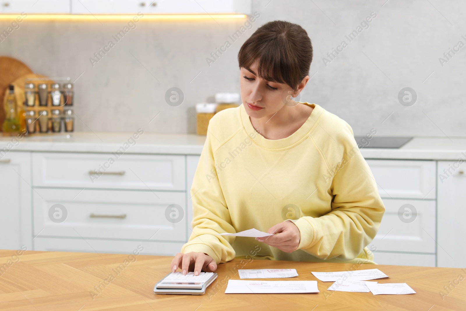 Photo of Paying bills. Woman with different invoices and calculator at wooden table indoors, space for text