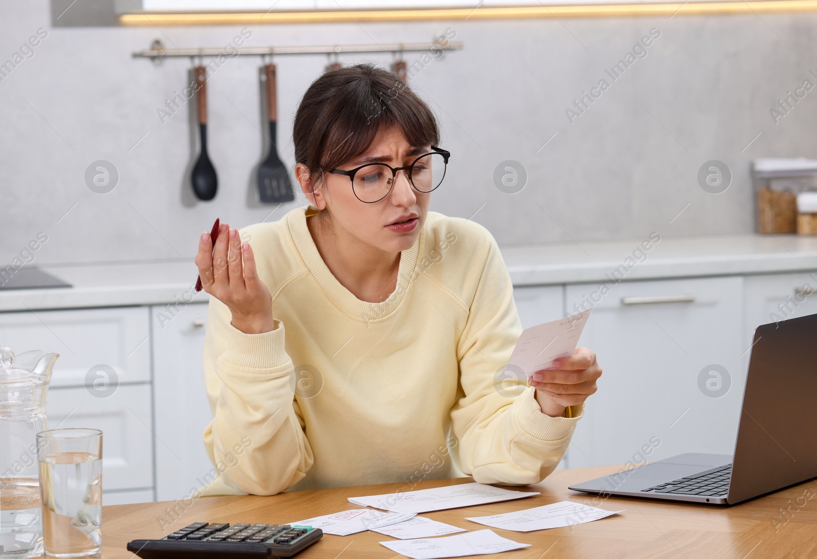 Photo of Paying bills. Upset woman with different invoices and calculator at wooden table indoors