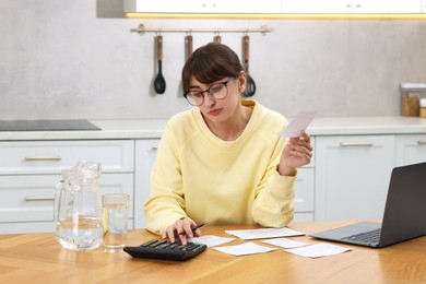 Photo of Paying bills. Woman with different invoices and calculator at wooden table indoors