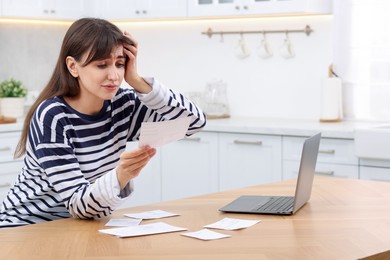 Photo of Paying bills. Upset woman with different invoices and laptop at wooden table indoors