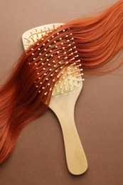 Photo of Wooden brush and lock of hair on brown background, top view