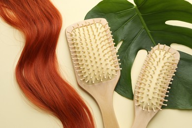 Photo of Wooden brushes, lock of hair and monstera leaf on beige background, flat lay