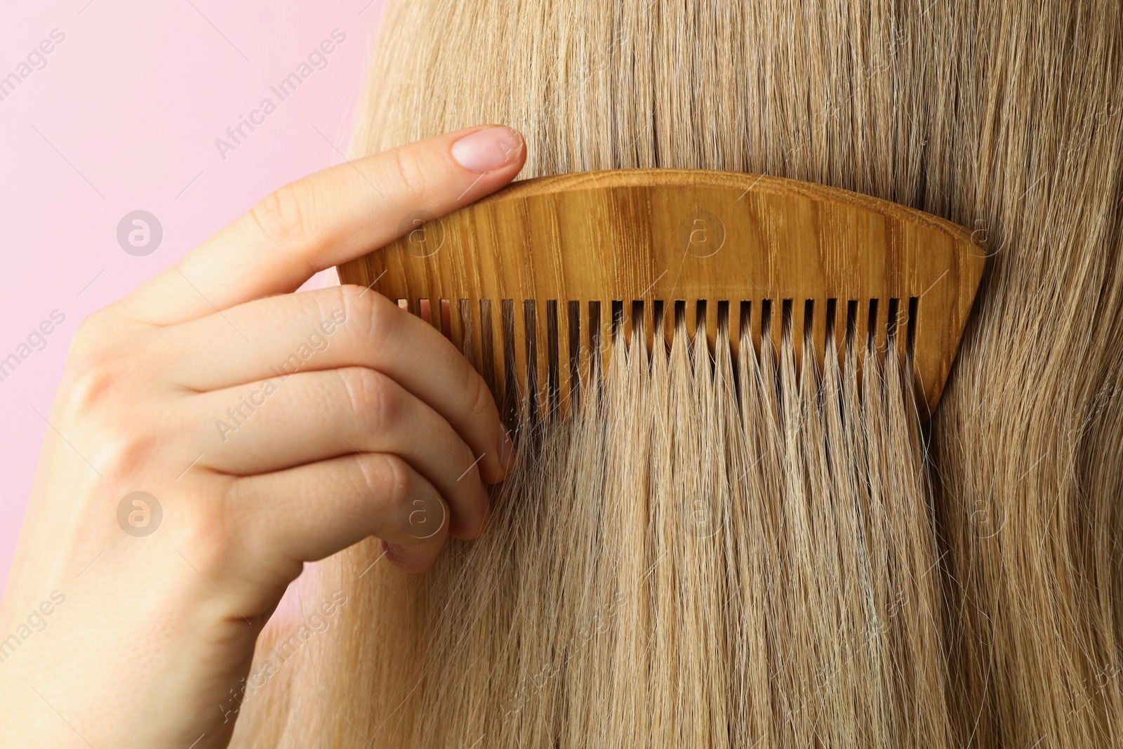 Photo of Woman brushing hair with wooden comb on pink background, closeup