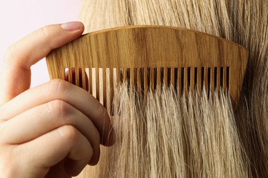 Photo of Woman brushing hair with wooden comb on pink background, closeup