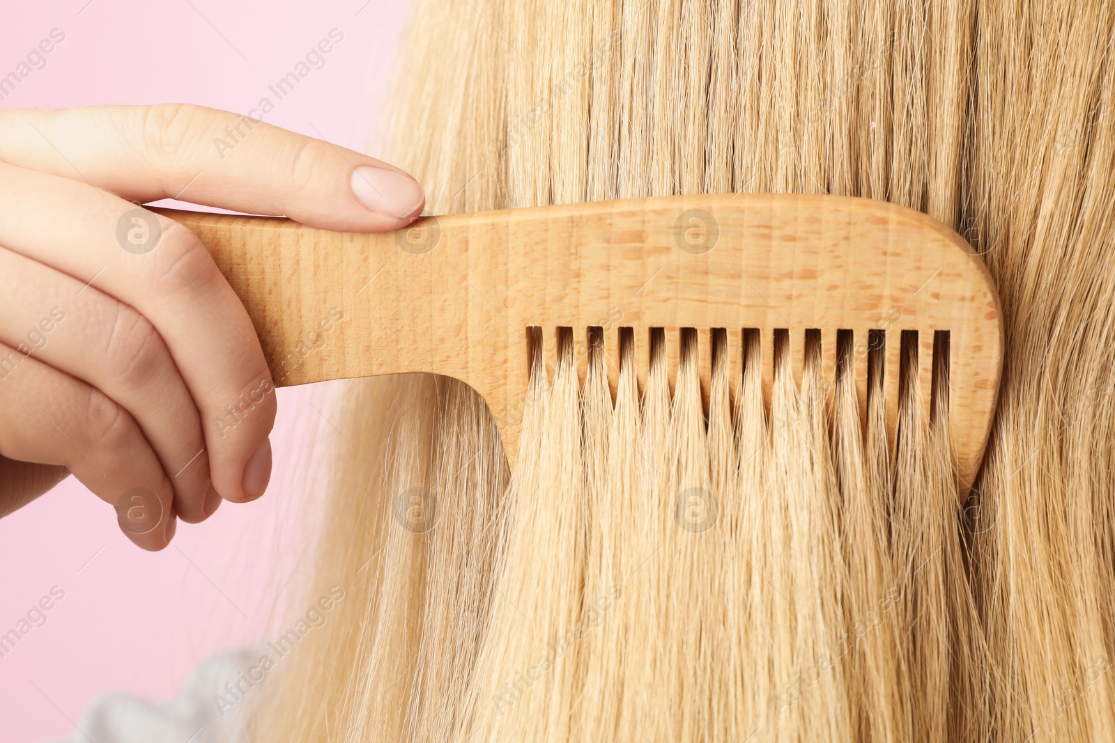 Photo of Woman brushing hair with wooden comb on pink background, closeup