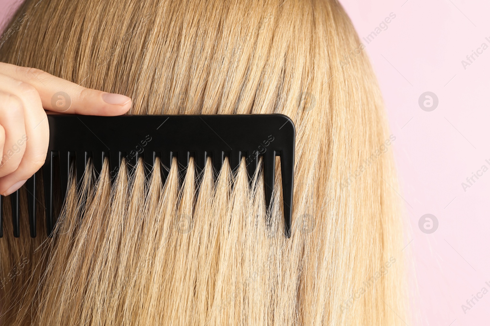 Photo of Woman brushing hair with plastic comb on pink background, closeup