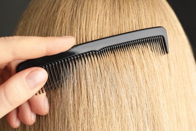 Photo of Woman brushing hair with plastic comb on grey background, closeup