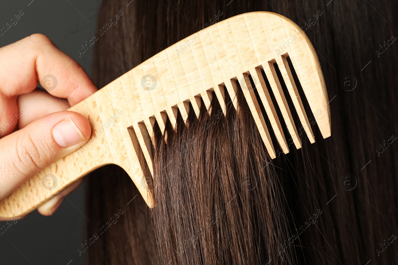 Photo of Woman brushing hair with wooden comb on grey background, closeup